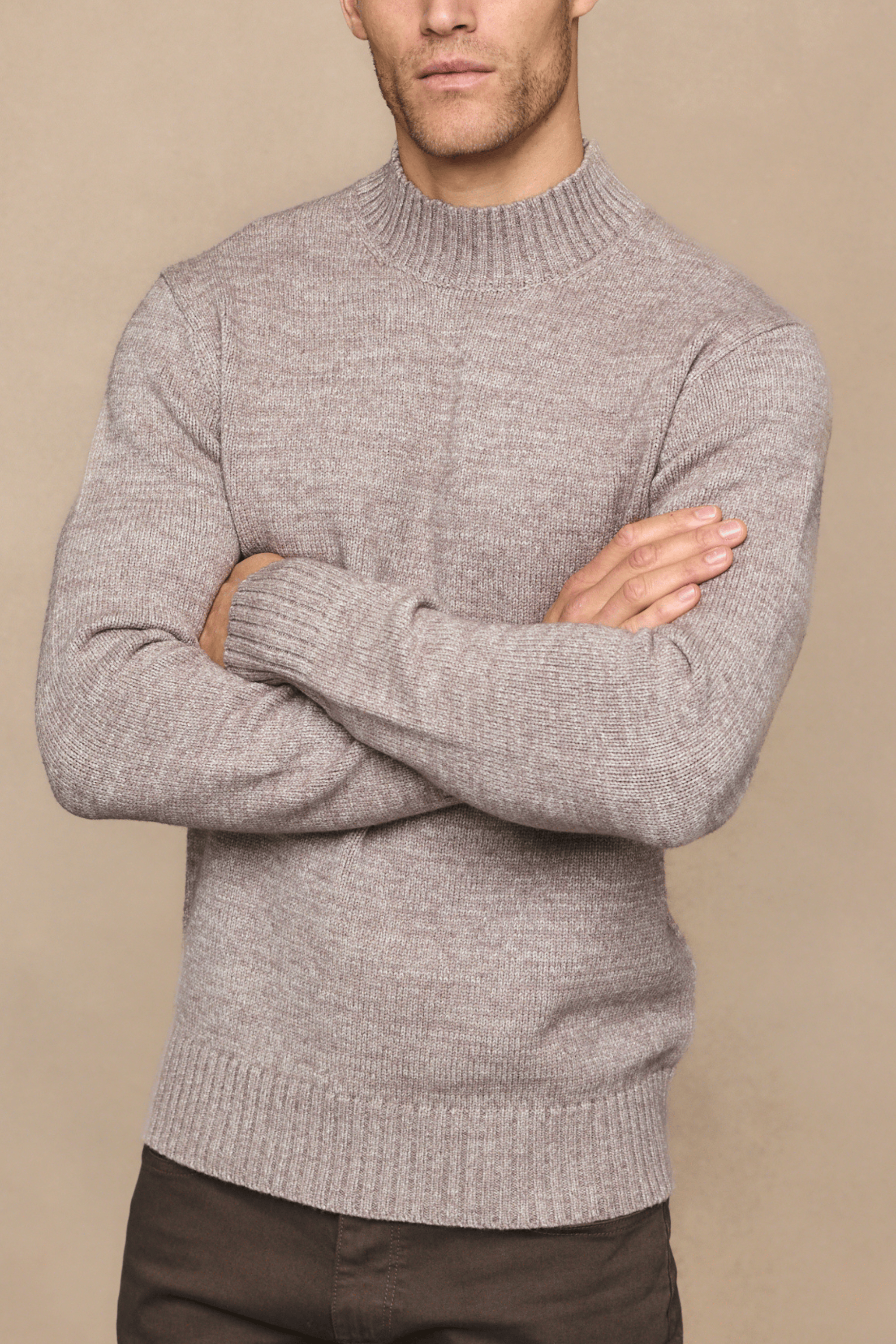 Man wearing a gray sweater with arms crossed against a beige background